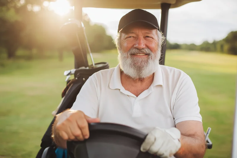 Senior man smiling while driving a golf cart on a green course