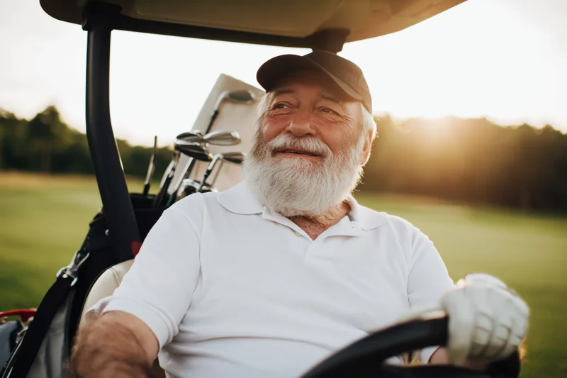 Senior man smiling while driving a golf cart on a golf course at sunset