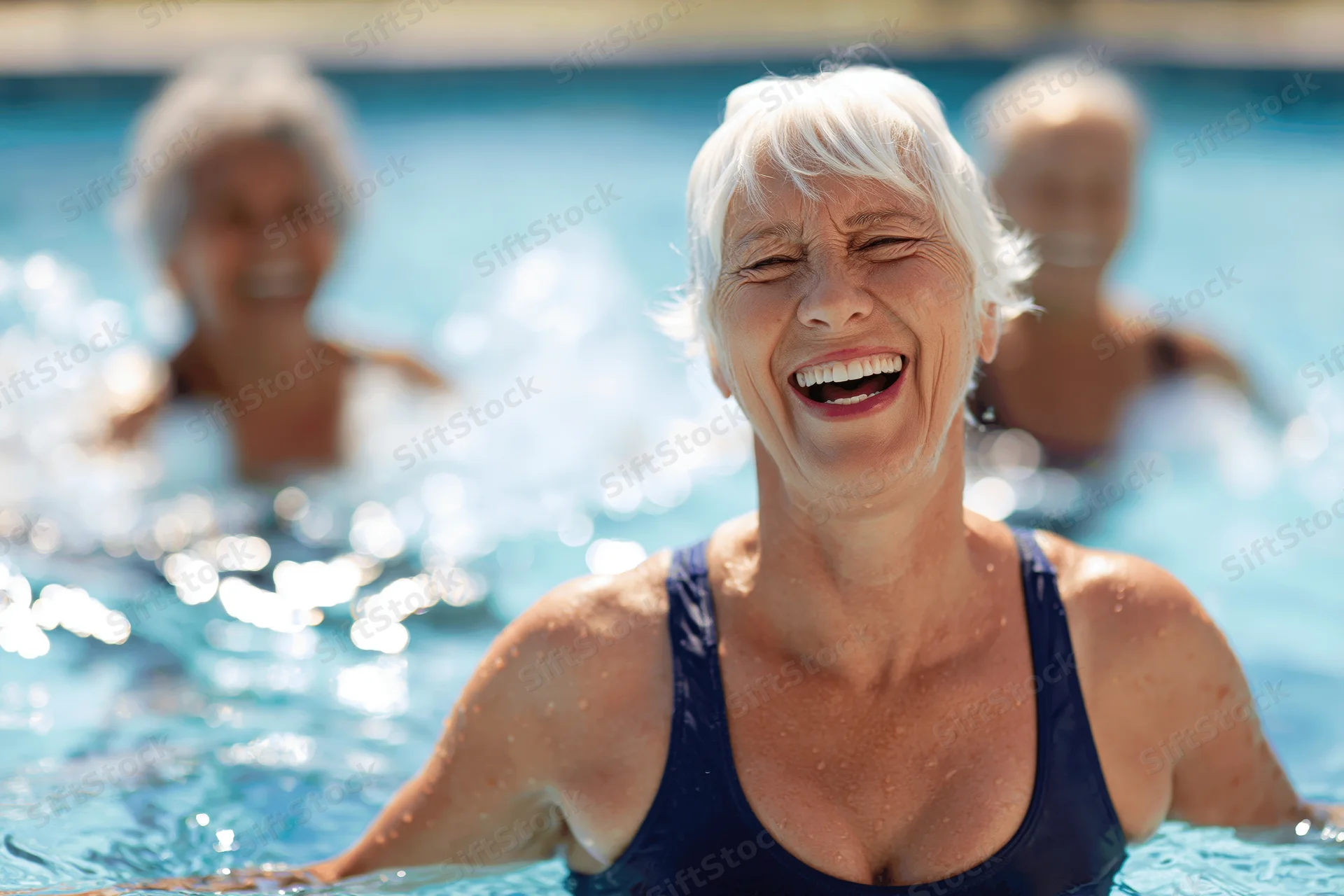 Senior woman laughing in a swimming pool with others in the background