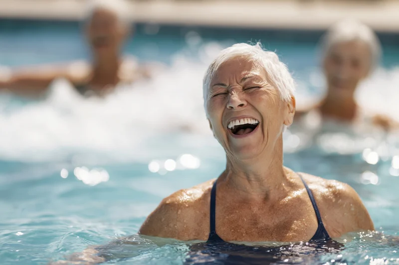 Senior woman laughing in a swimming pool with others in the background