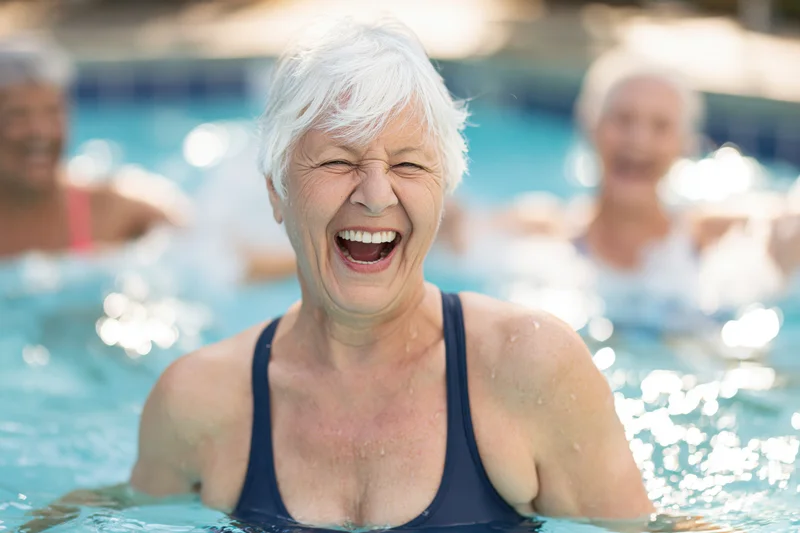 Senior woman laughing in a swimming pool with others in the background