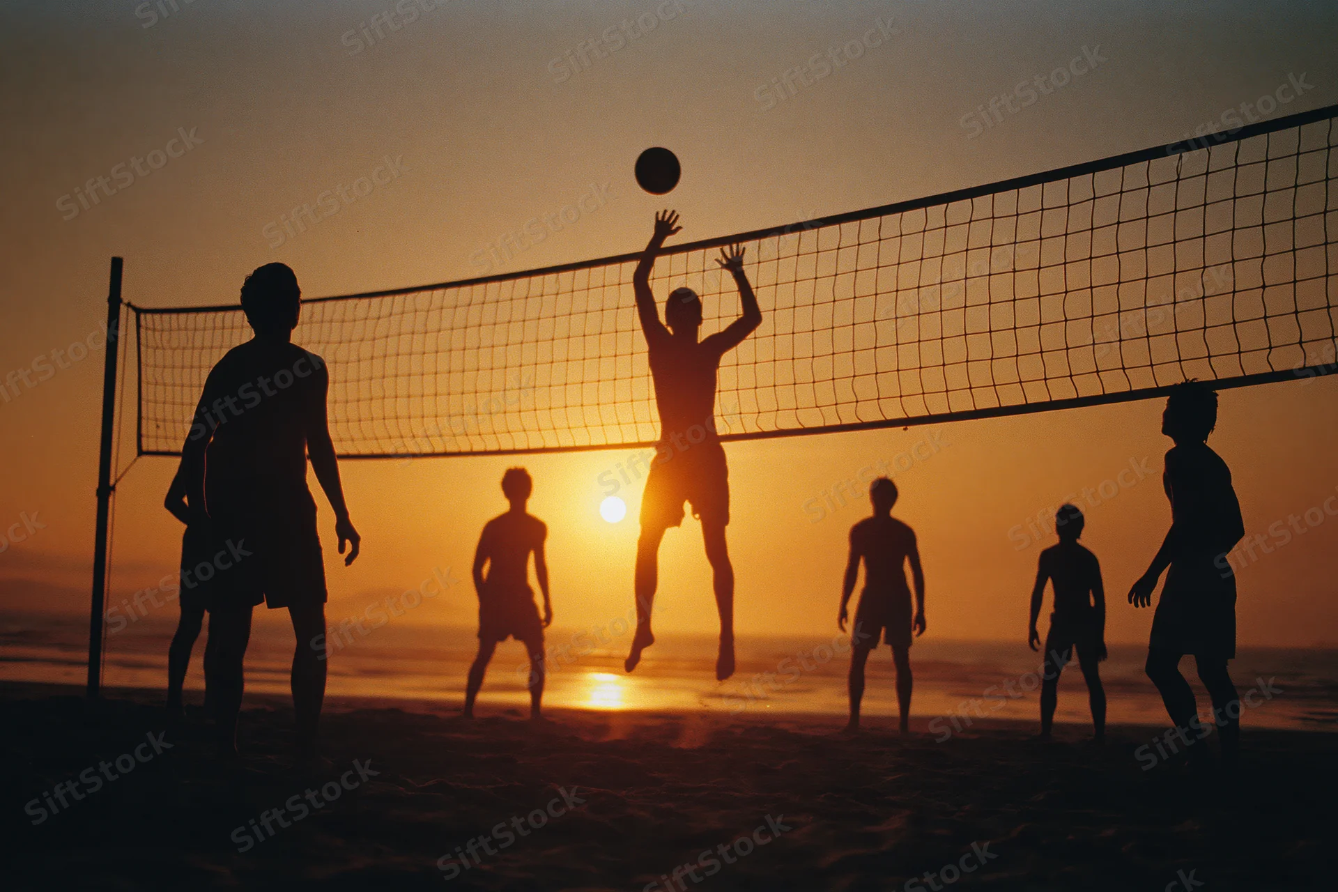 Silhouettes of young men playing beach volleyball at sunset on the sand
