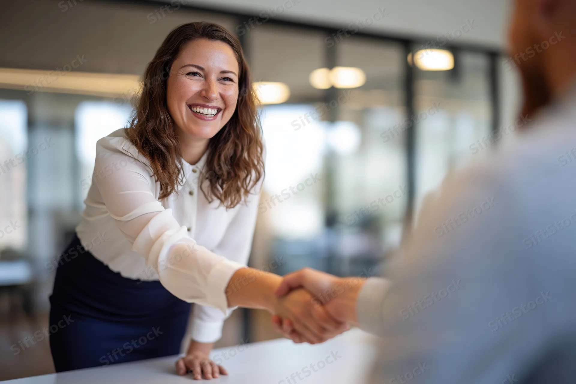 Smiling businesswoman shaking hands with a man at a desk in an office