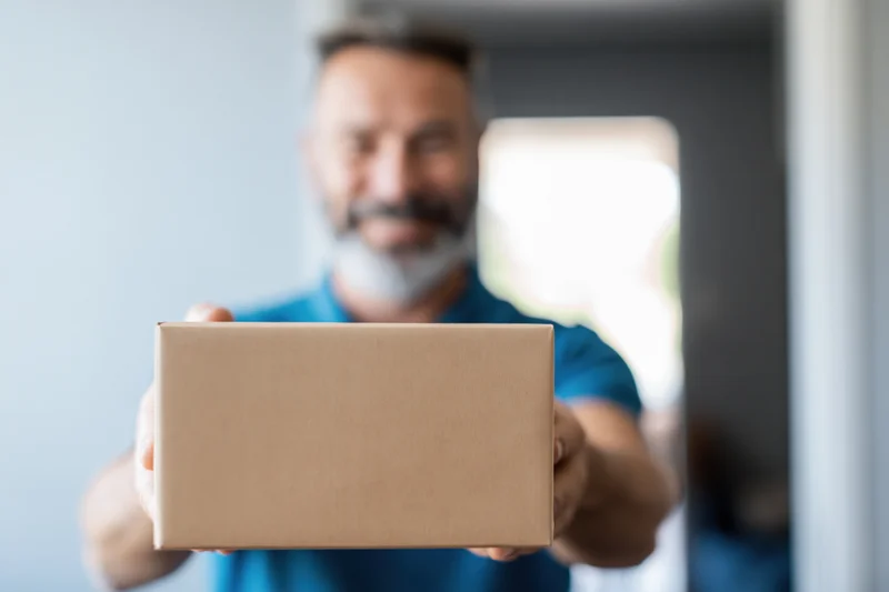Delivery man holding a cardboard box at a doorway