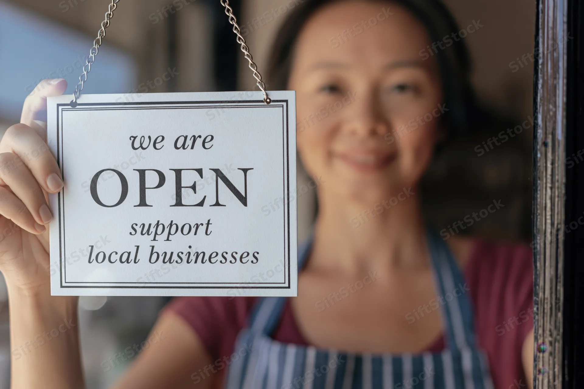 Woman in apron holding open sign at shop window