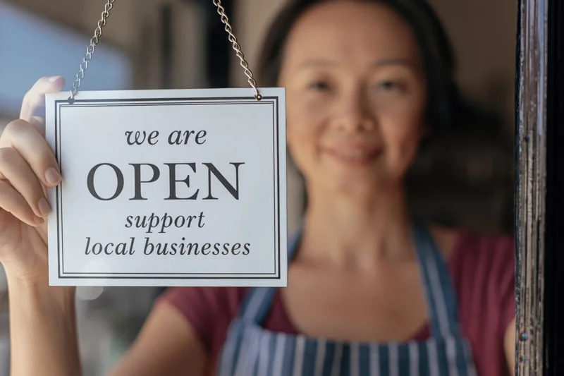 Woman in apron holding open sign at shop window
