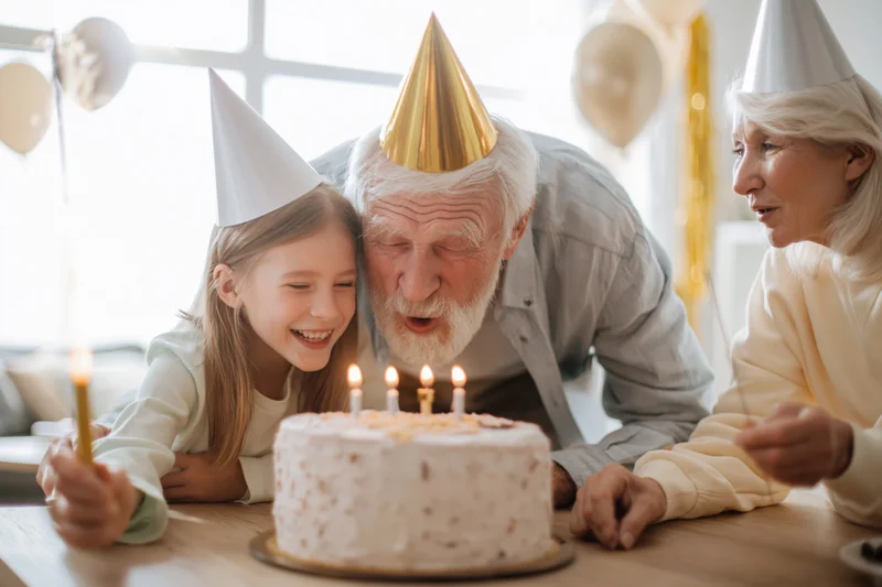 Three-generation family blowing candles on birthday cake at home