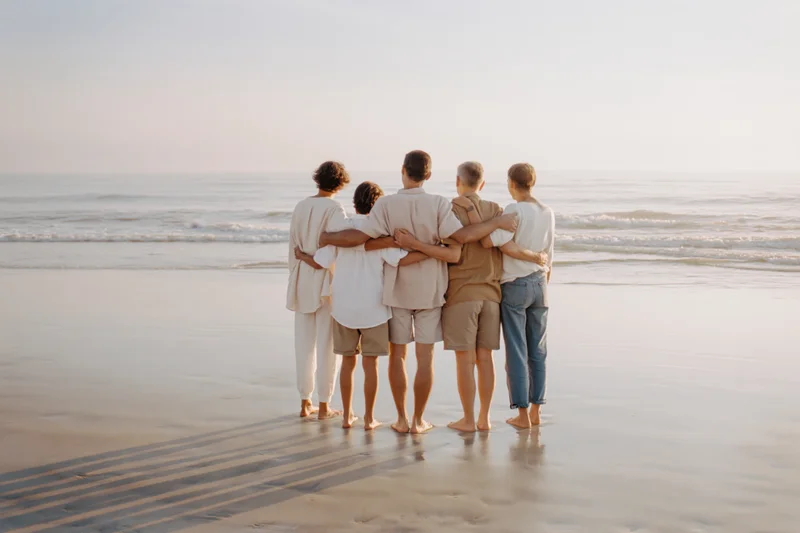 Three-generation family standing together on wet beach sand with arms around each other facing ocean