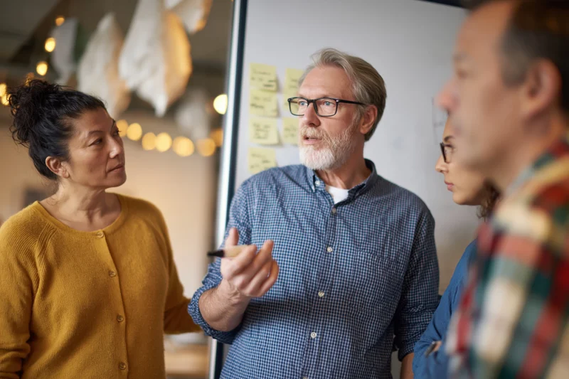 Three coworkers discussing ideas around a whiteboard in an office meeting space