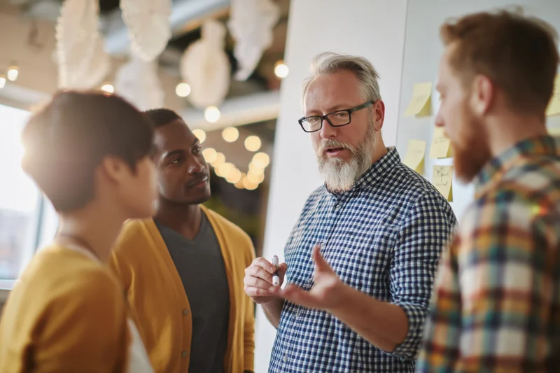 Four coworkers discussing ideas around a whiteboard in an office meeting space