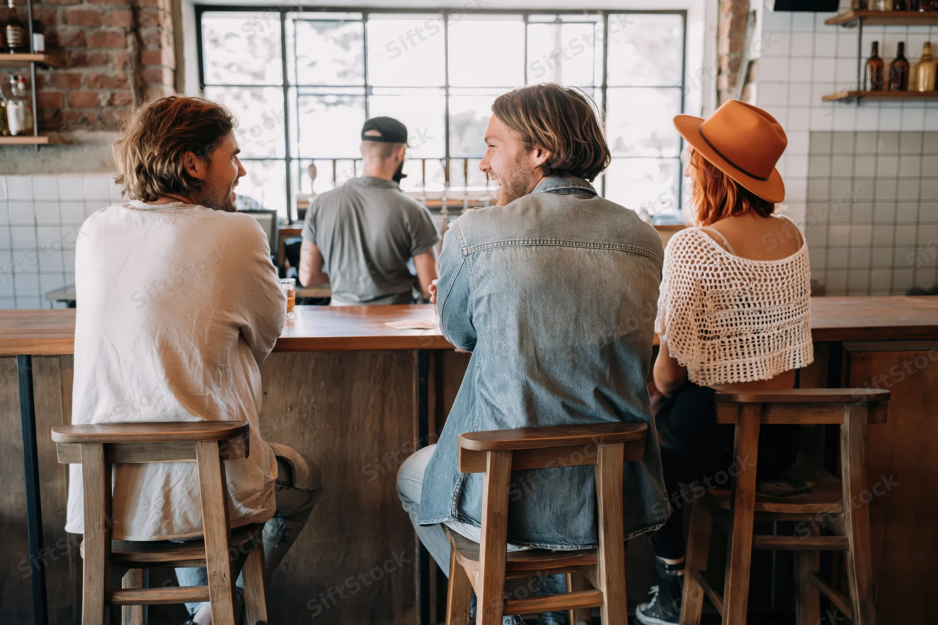Three friends sitting on wooden bar stools at a cafe counter conversing