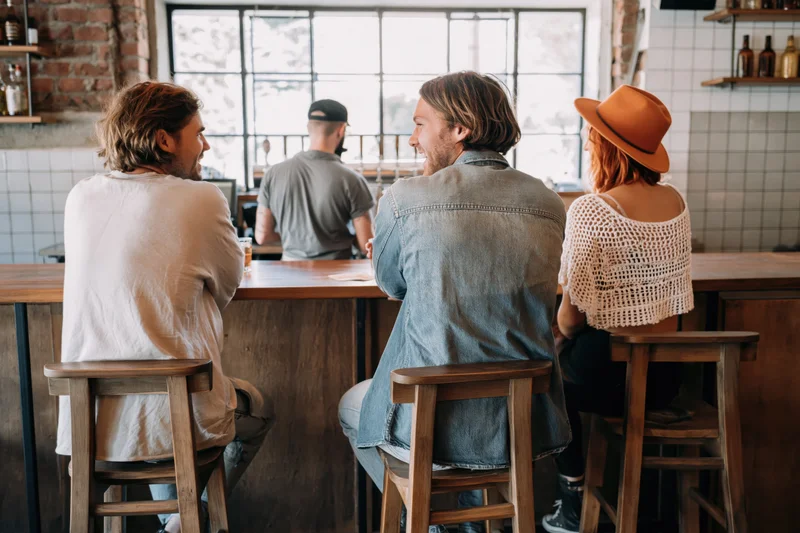 Three friends sitting on wooden bar stools at a cafe counter conversing