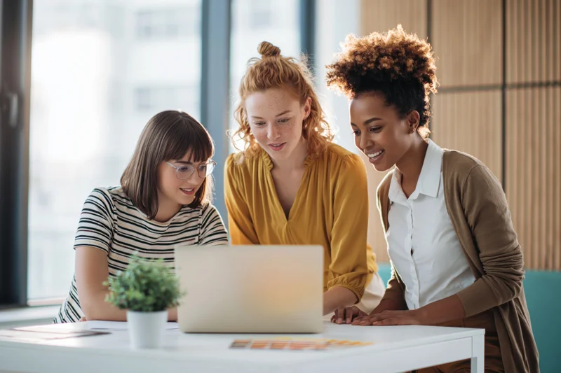 Three young women collaborating around a laptop in a bright office