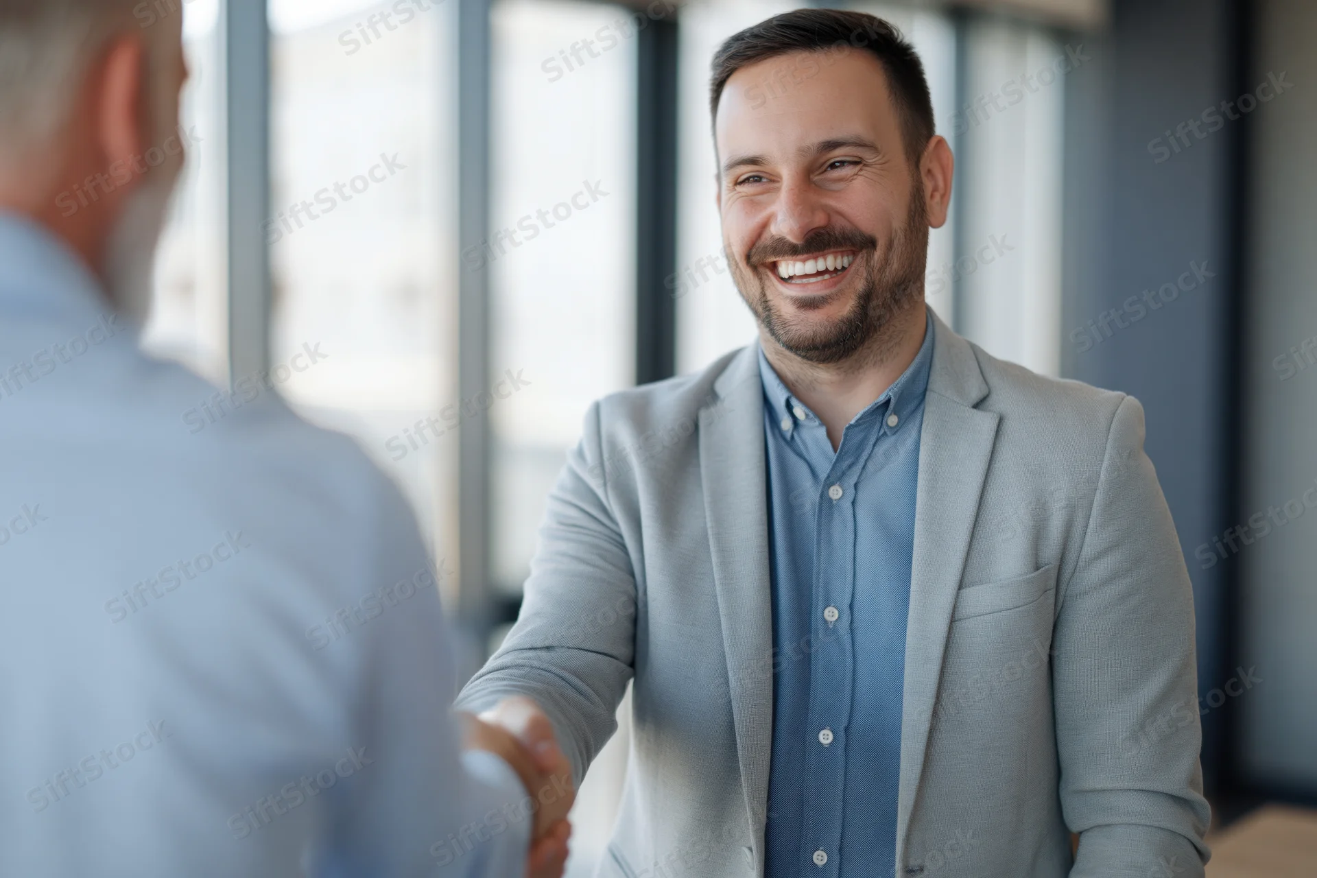 Businessman smiling while shaking hands with another man in a modern office