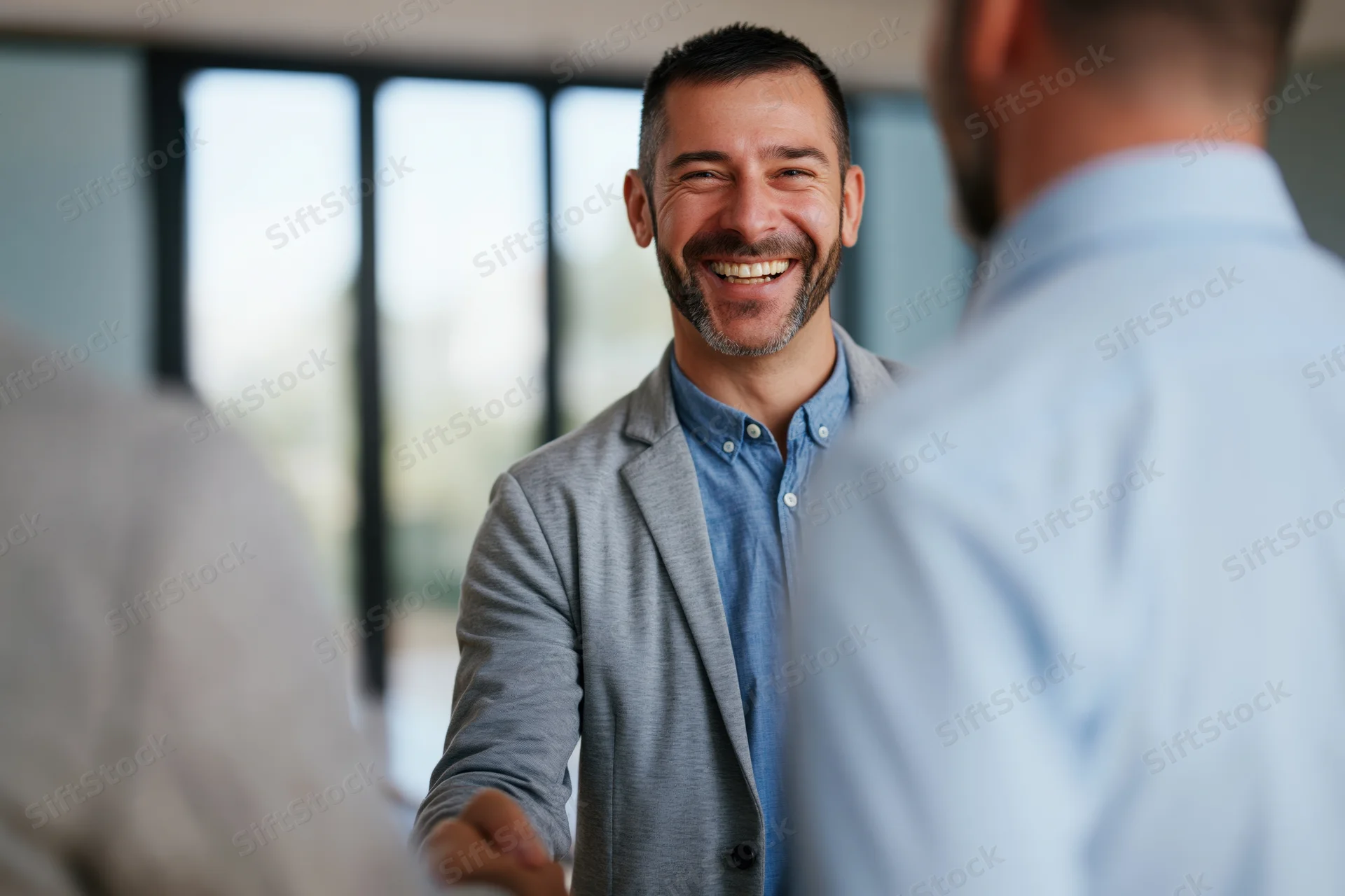 Businessman smiling during handshake in modern office with colleagues