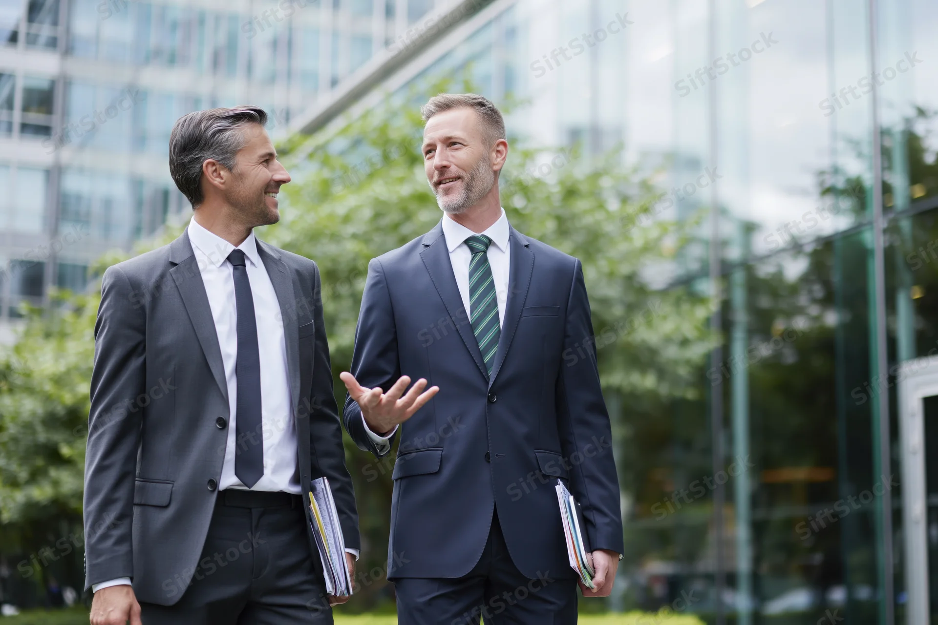 Two businessmen in suits walking and talking outside a modern glass office building