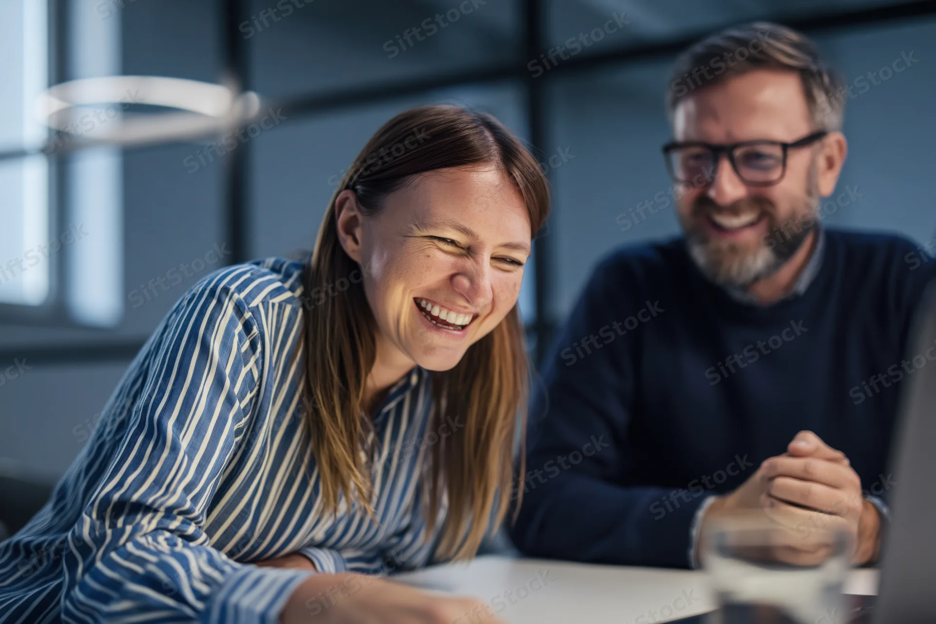 Woman and man laughing during video call on laptop in office