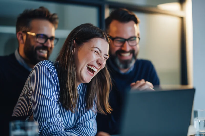 Woman laughing with coworkers during video call on laptop in office