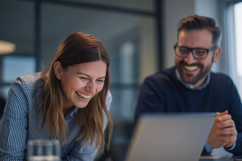 Woman and man laughing during video call on laptop in office