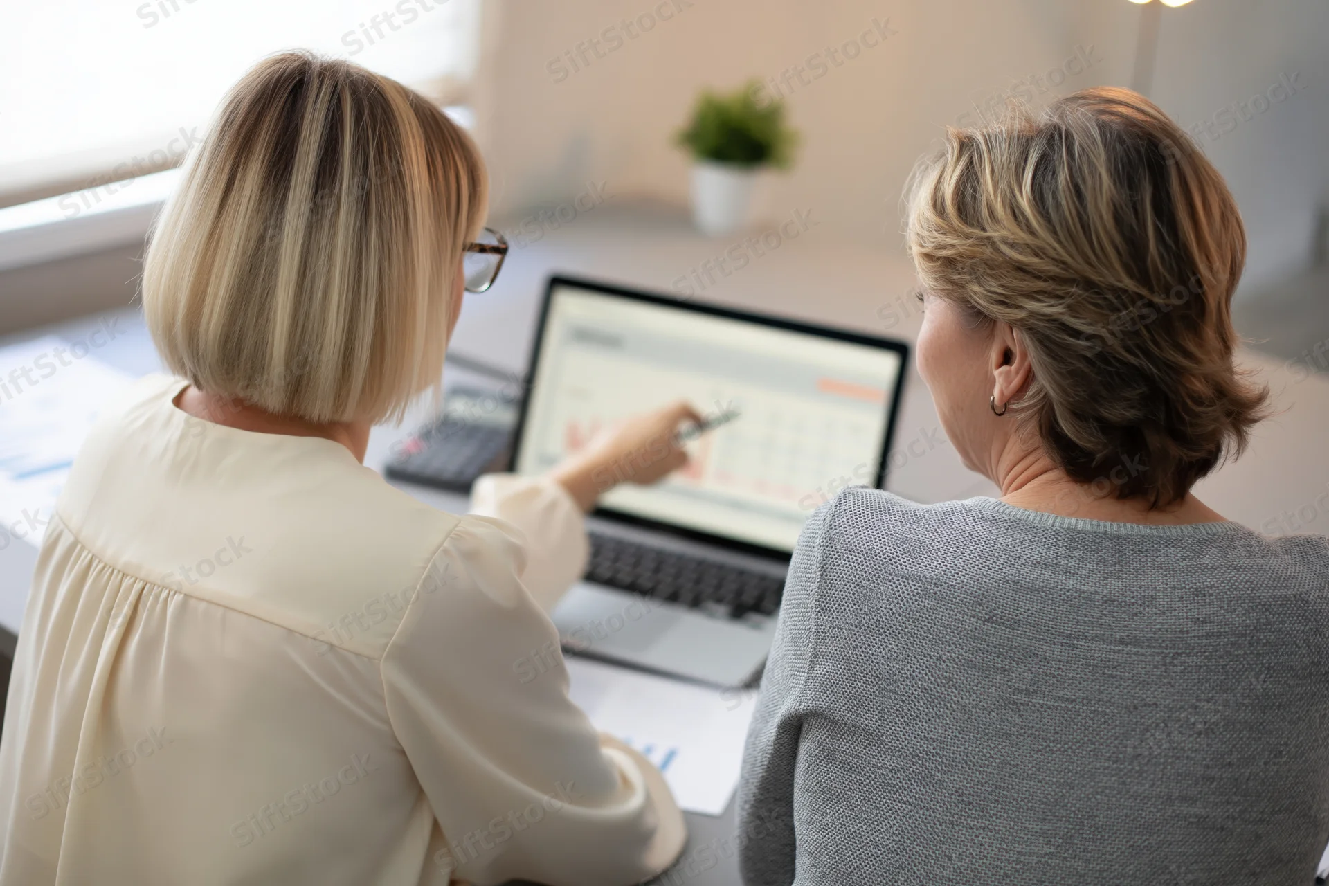 Two women reviewing financial data on a laptop at a desk in an office