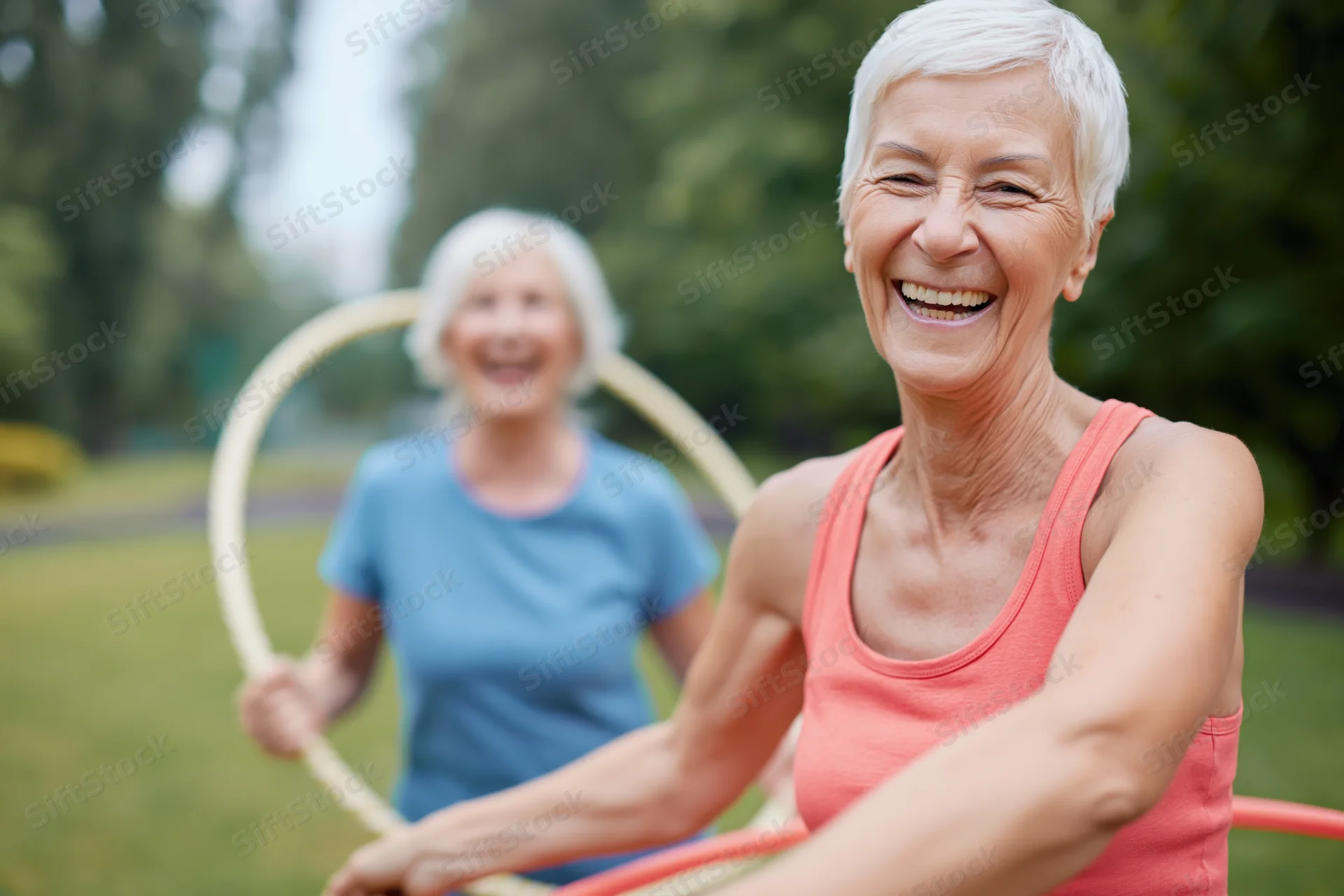 Senior woman laughing while exercising with a hula hoop in a park