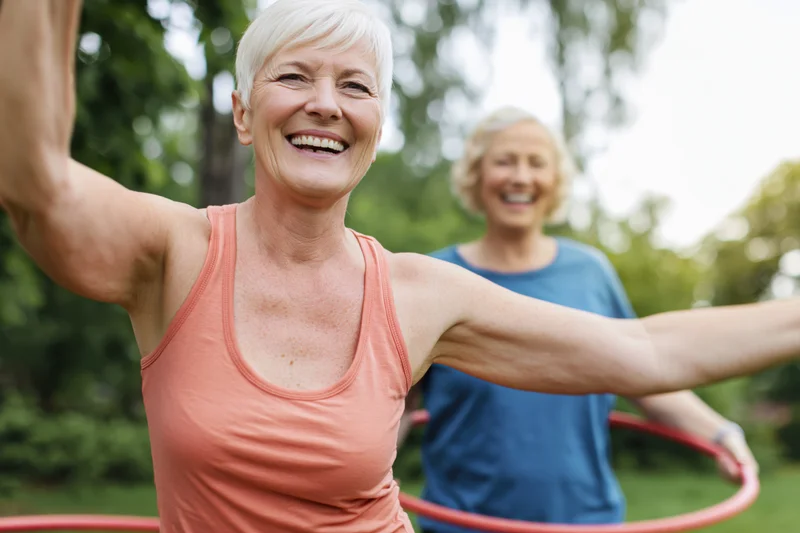 Senior woman smiling with arms outstretched while exercising with a hula hoop in a park