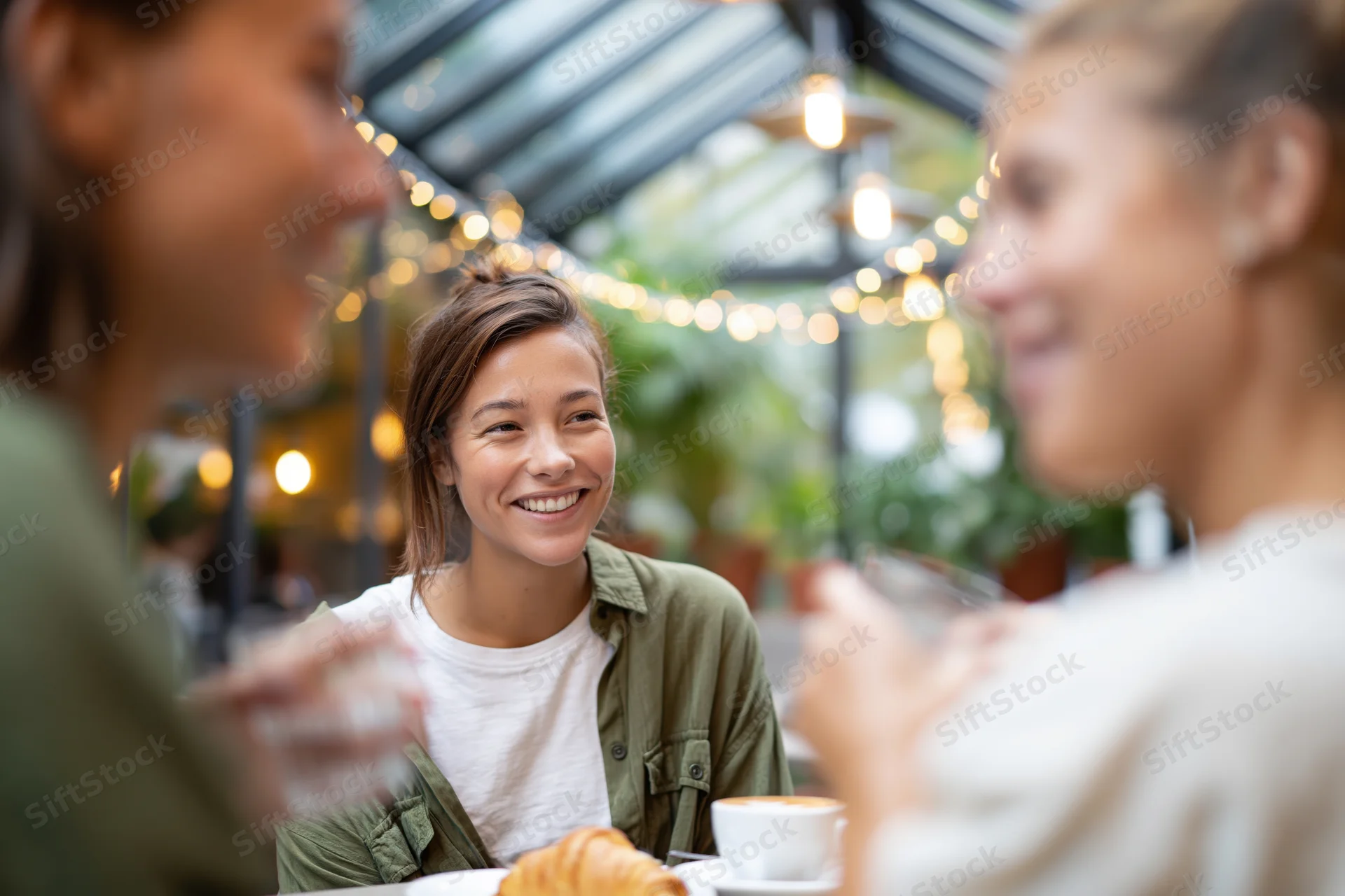 Woman smiling during conversation with friends at cafe table outdoors