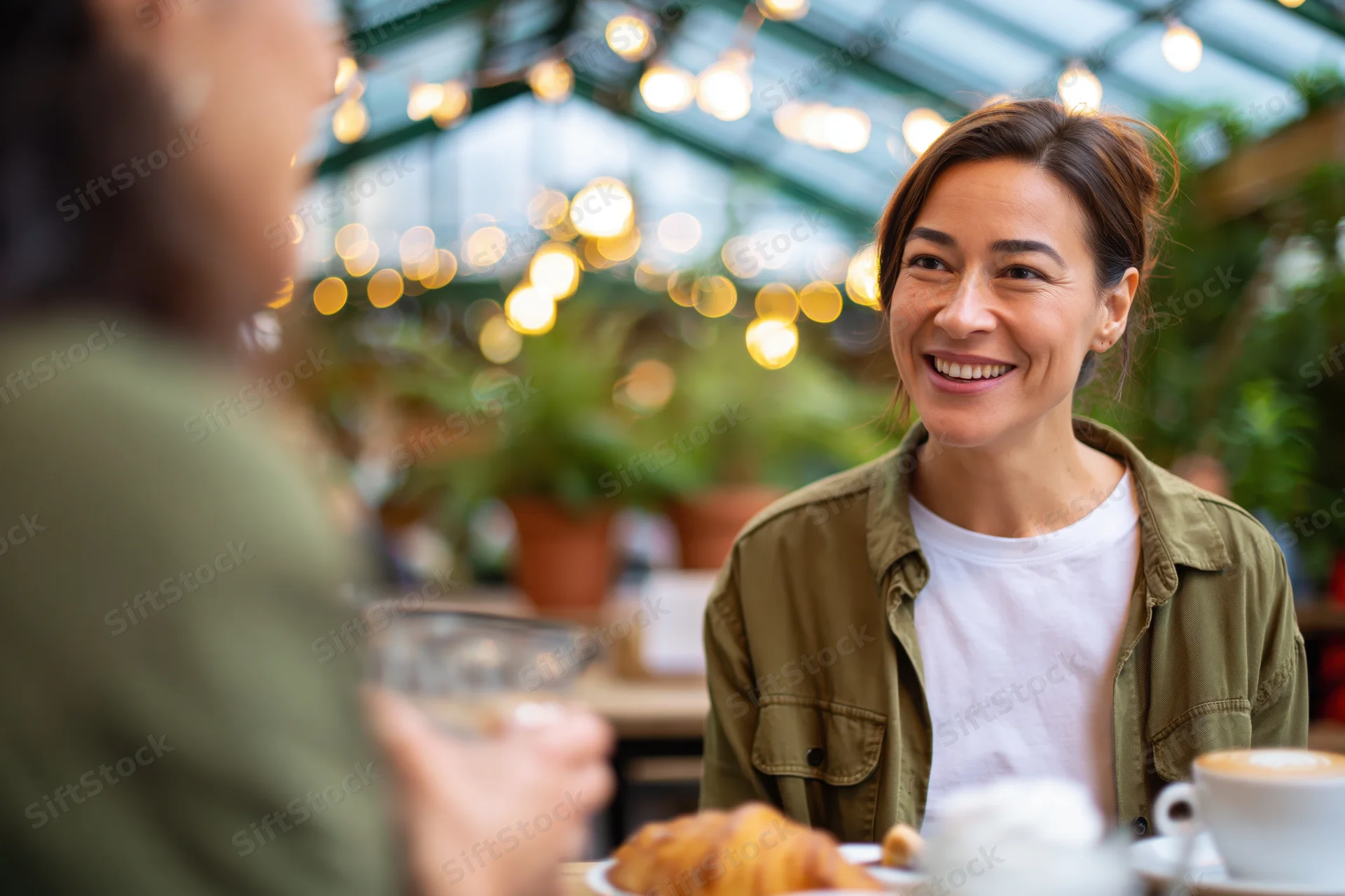 Woman smiling while chatting with a friend over coffee at a cafe table