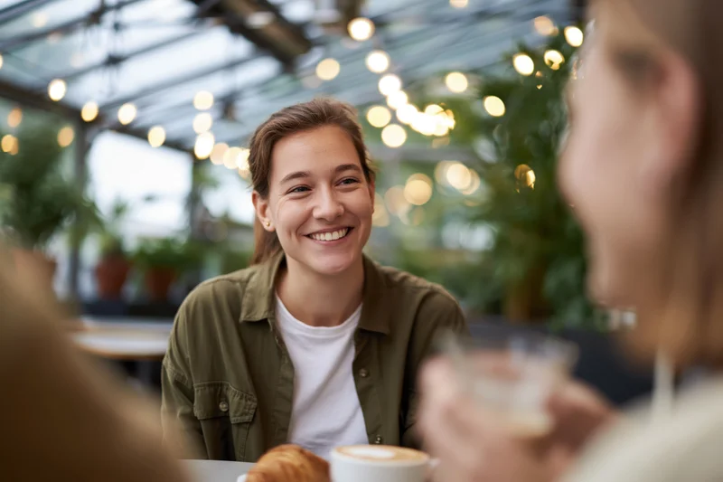 Woman smiling while chatting with friend over coffee at cafe table