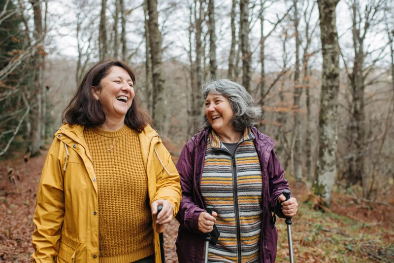 Two women laughing while hiking together on a forest trail in autumn