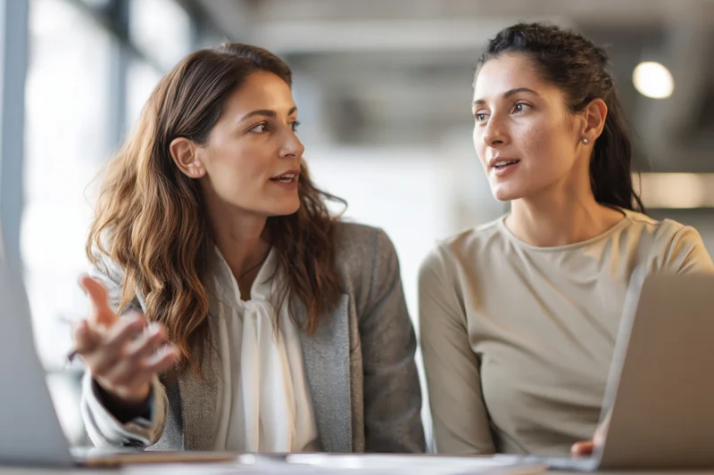 Two women discussing work at laptops in an office meeting