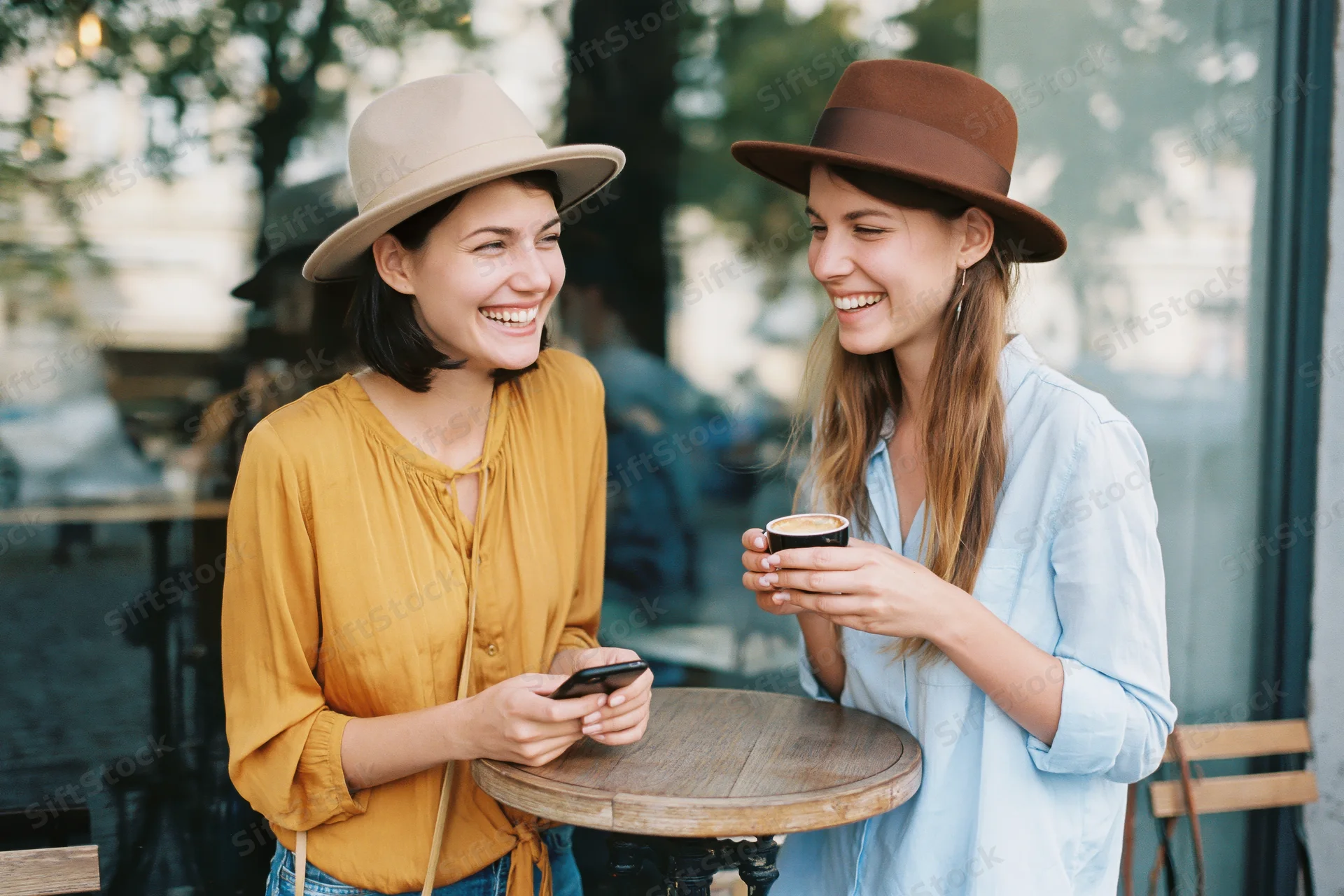 Two young women laughing together at an outdoor cafe table