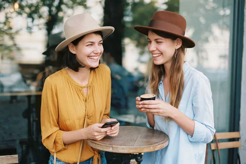 Two young women laughing together at an outdoor cafe table