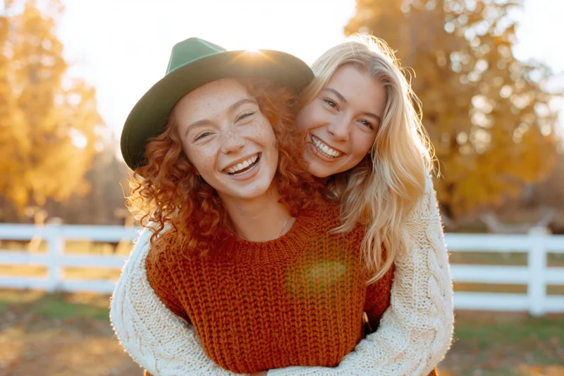 Two young women laughing during a piggyback ride in an autumn park