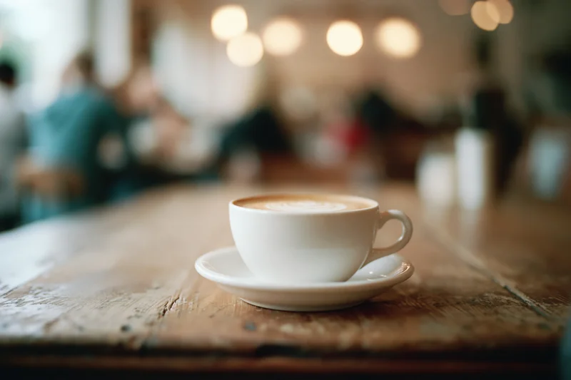 White ceramic latte cup with foam art on wooden table in cafe interior