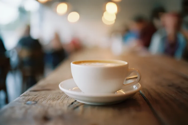 White ceramic latte cup with foam art on wooden table in cafe interior