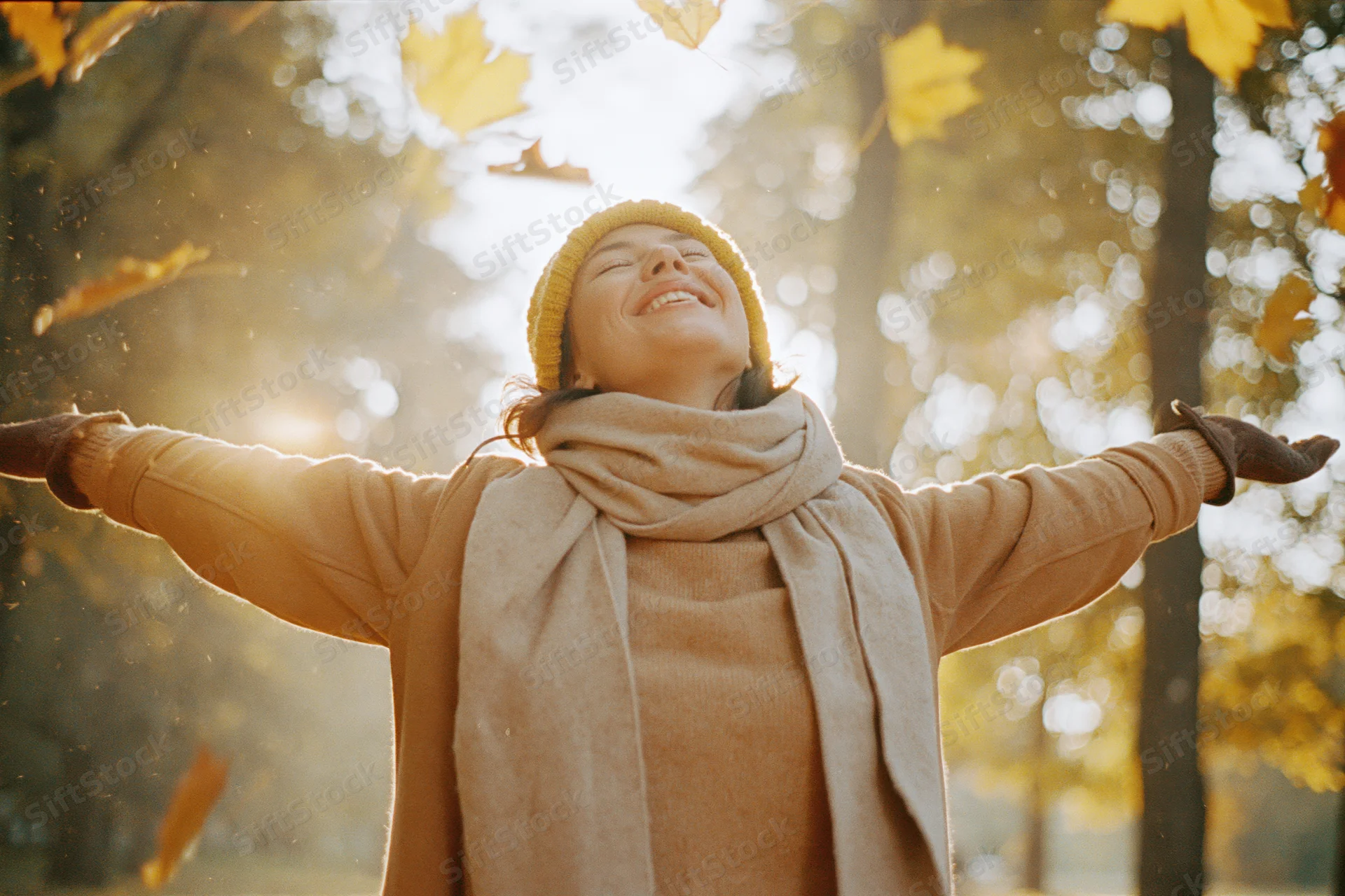 Woman laughing with arms outstretched in autumn forest as leaves fall around her