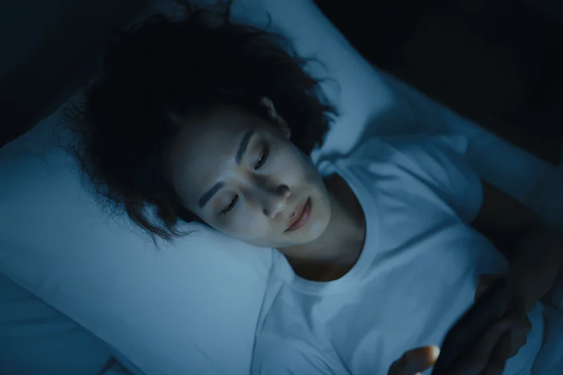 Young asian woman lying in bed at night staring at her smartphone screen