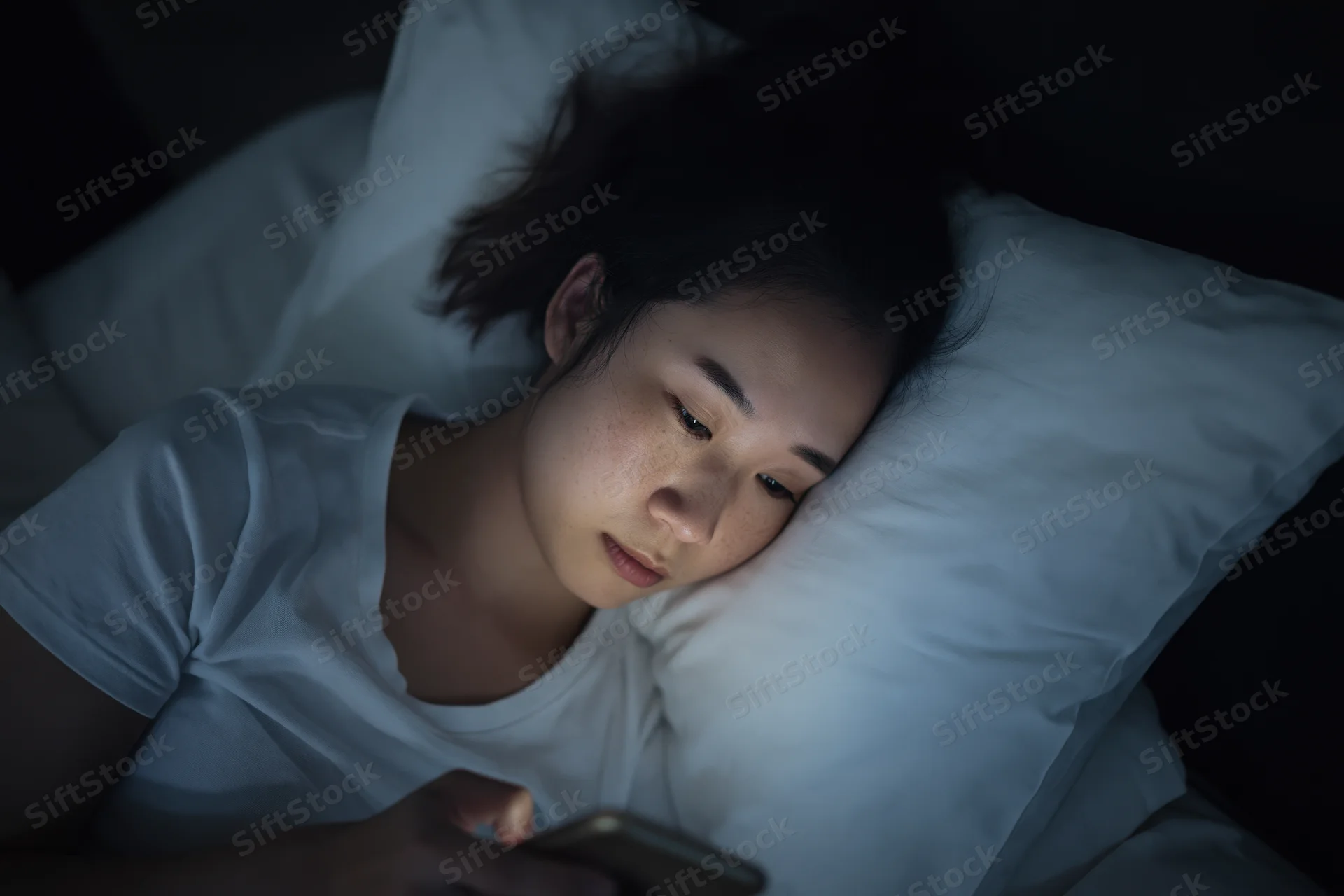 Young asian woman lying in bed at night staring at her smartphone screen