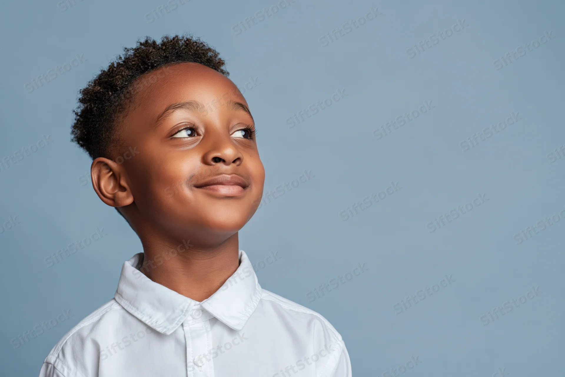Young black boy smiling softly and looking upward in a studio portrait with copyspace