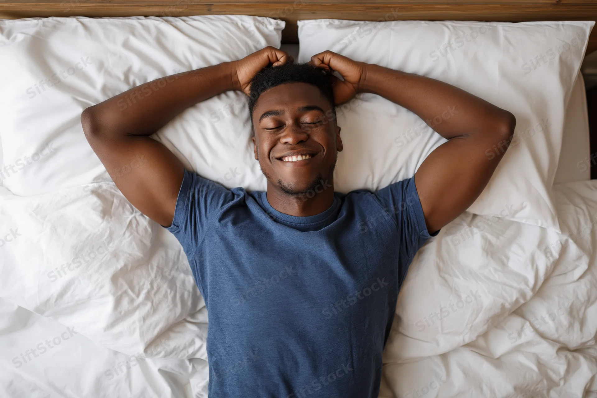 Young black man waking up in bed stretching arms above head with eyes closed and smiling