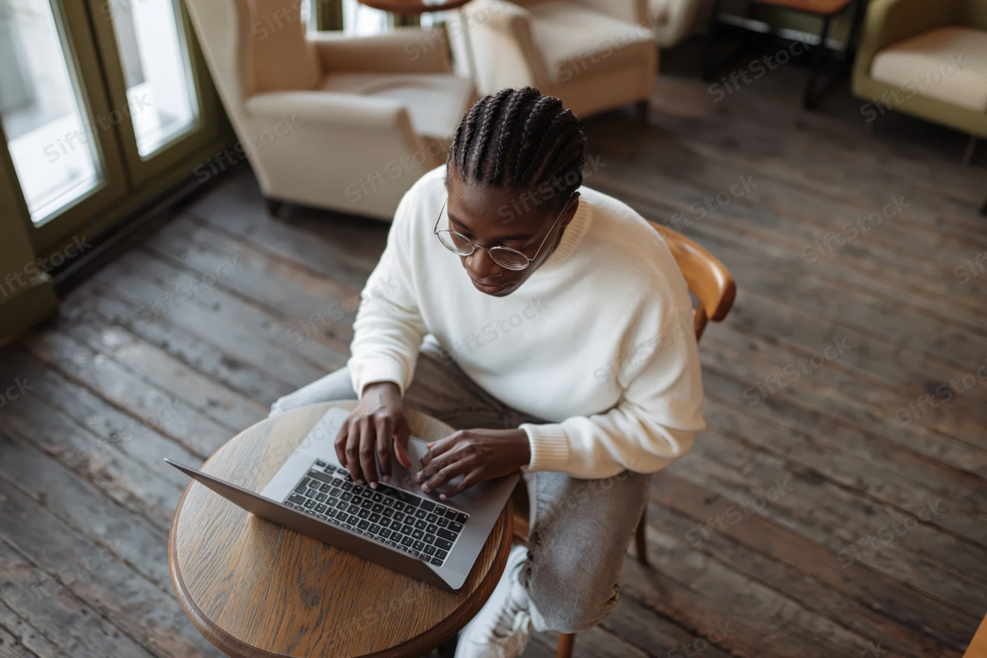 Young black man with braided hair working on laptop at wooden table in cafe