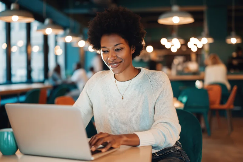 Young black woman with natural afro working on laptop at cafe table