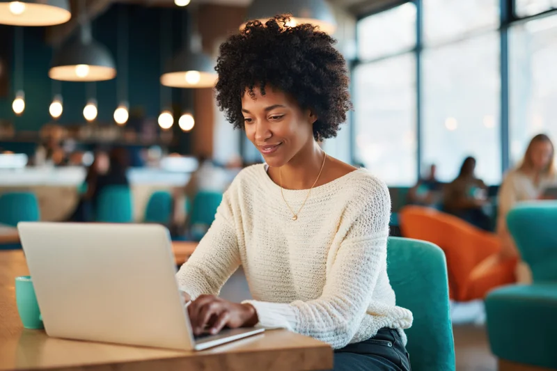 Young black woman with natural afro working on laptop in modern cafe interior