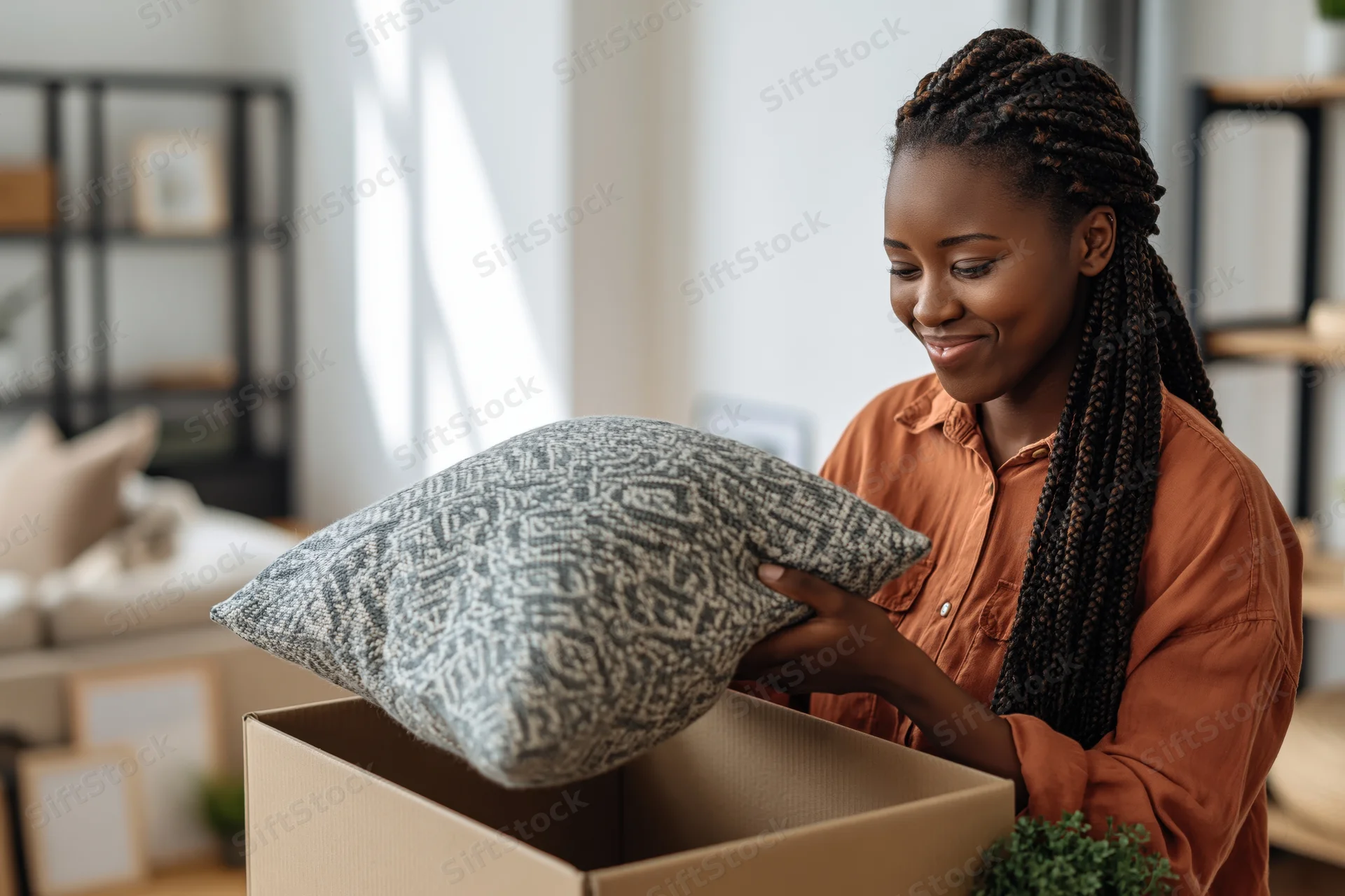 Young black woman unpacking a cushion from a cardboard box in a bright living room