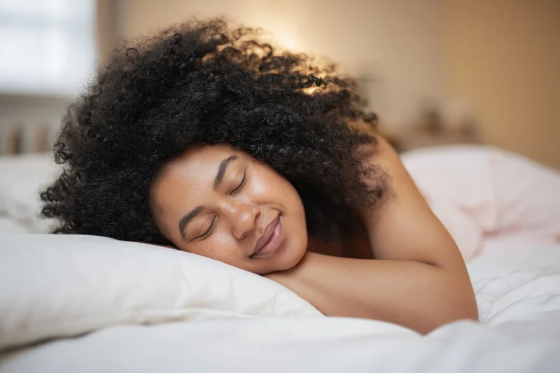 Young black woman sleeping peacefully in bed with voluminous curly hair resting on a white pillow