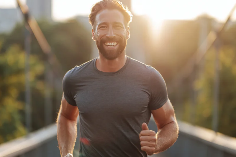 Man jogging across city bridge smiling at camera in golden hour light