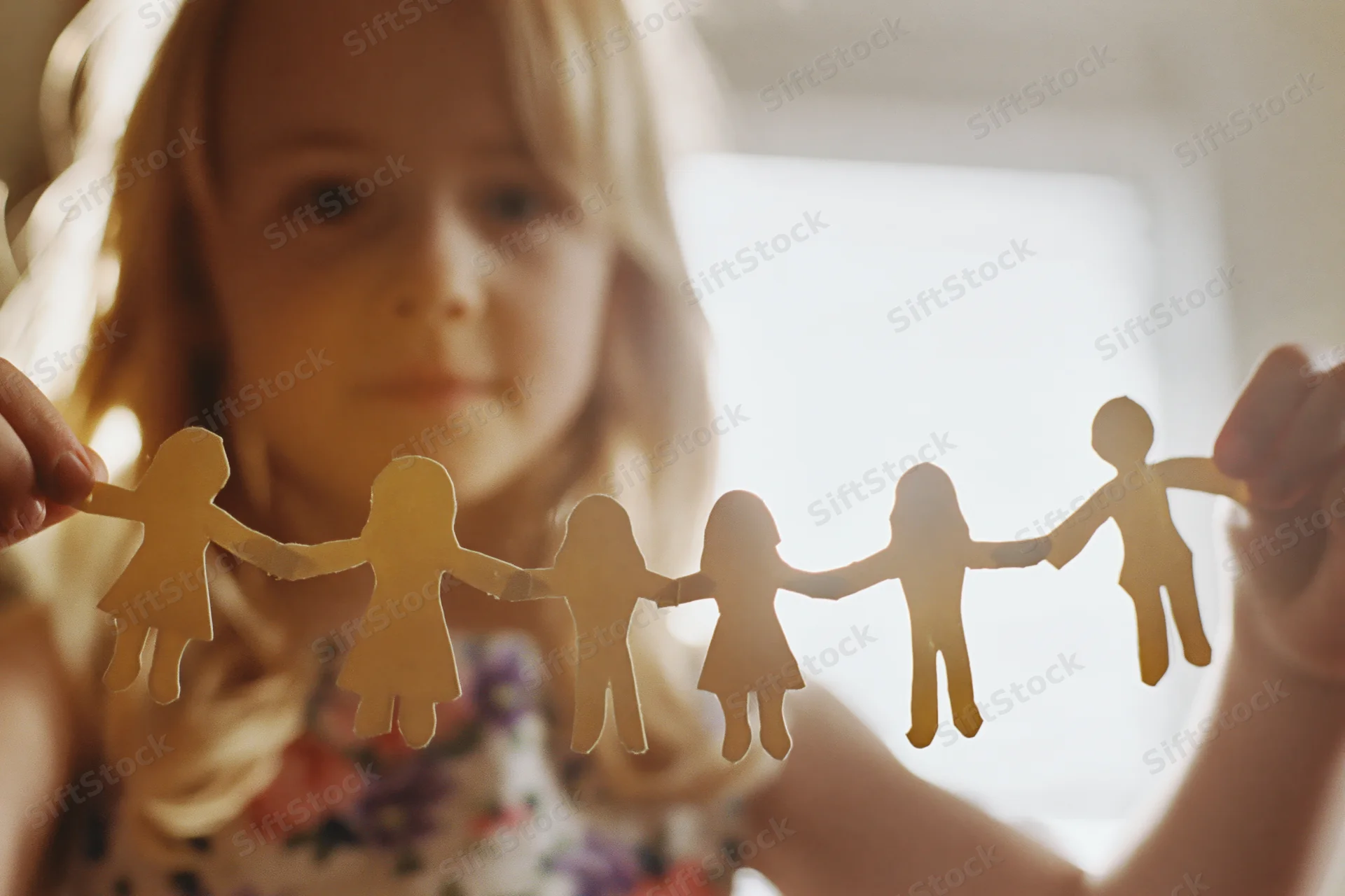 Young blonde girl holding a paper chain of cutout family figures indoors
