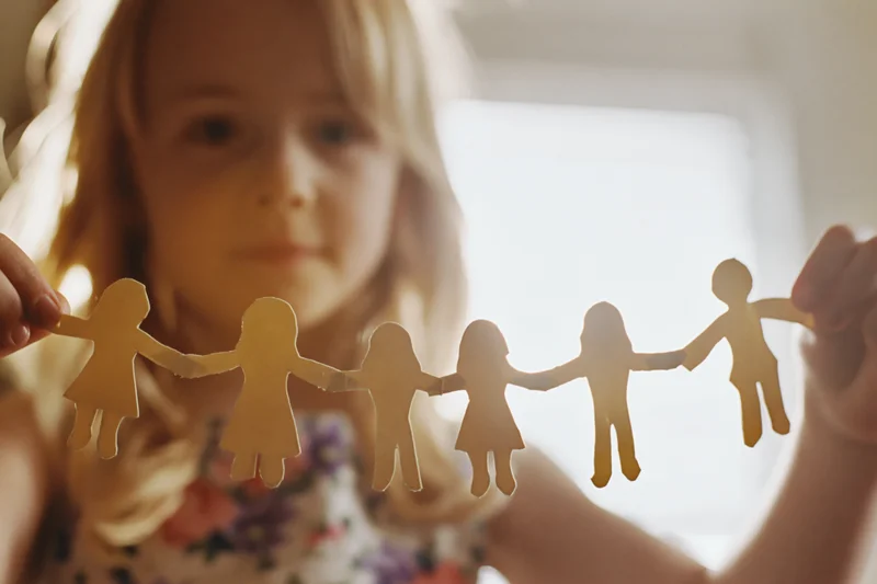 Young blonde girl holding a paper chain of cutout family figures indoors