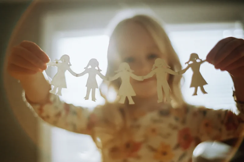 Young blonde girl holding a paper chain of family cutouts in front of a window